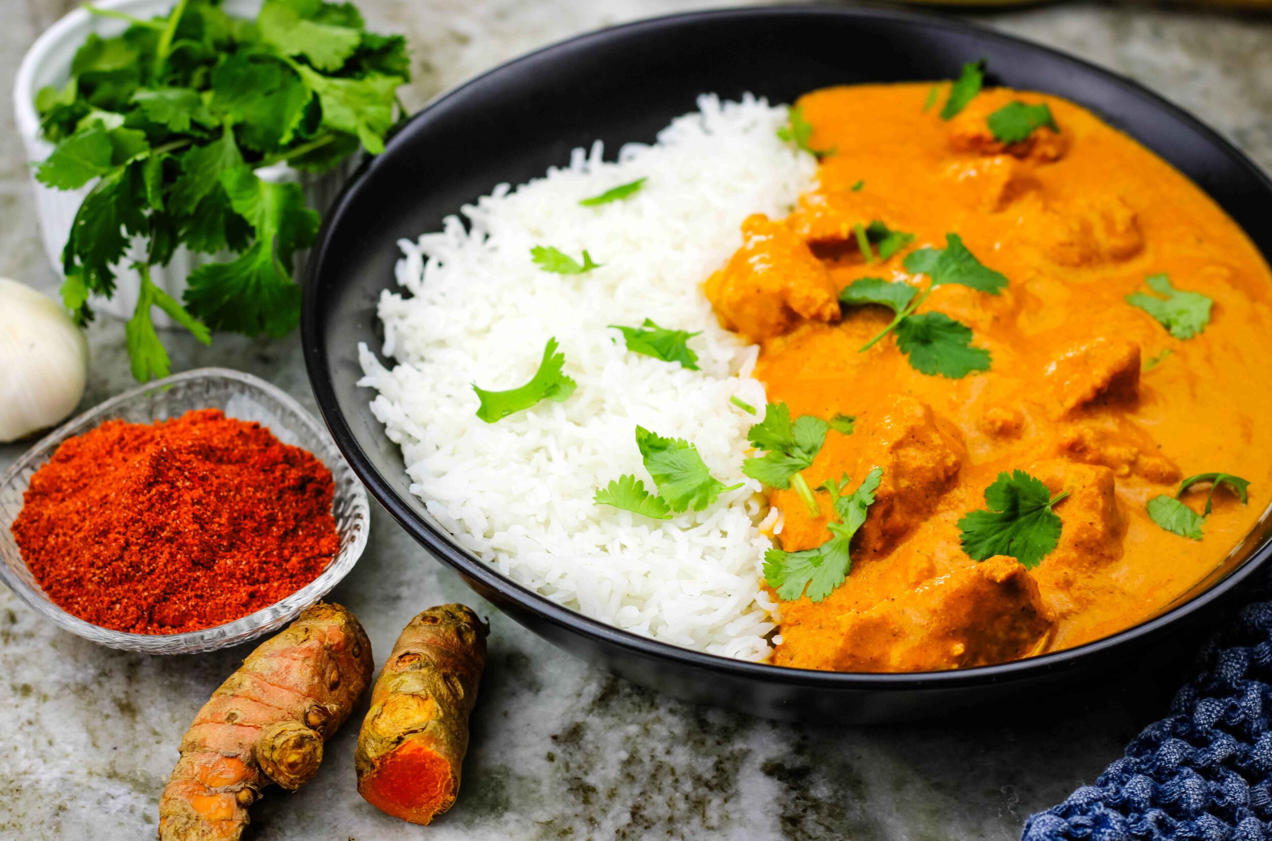 Butter chicken and rice in a dish surrounded by spices.