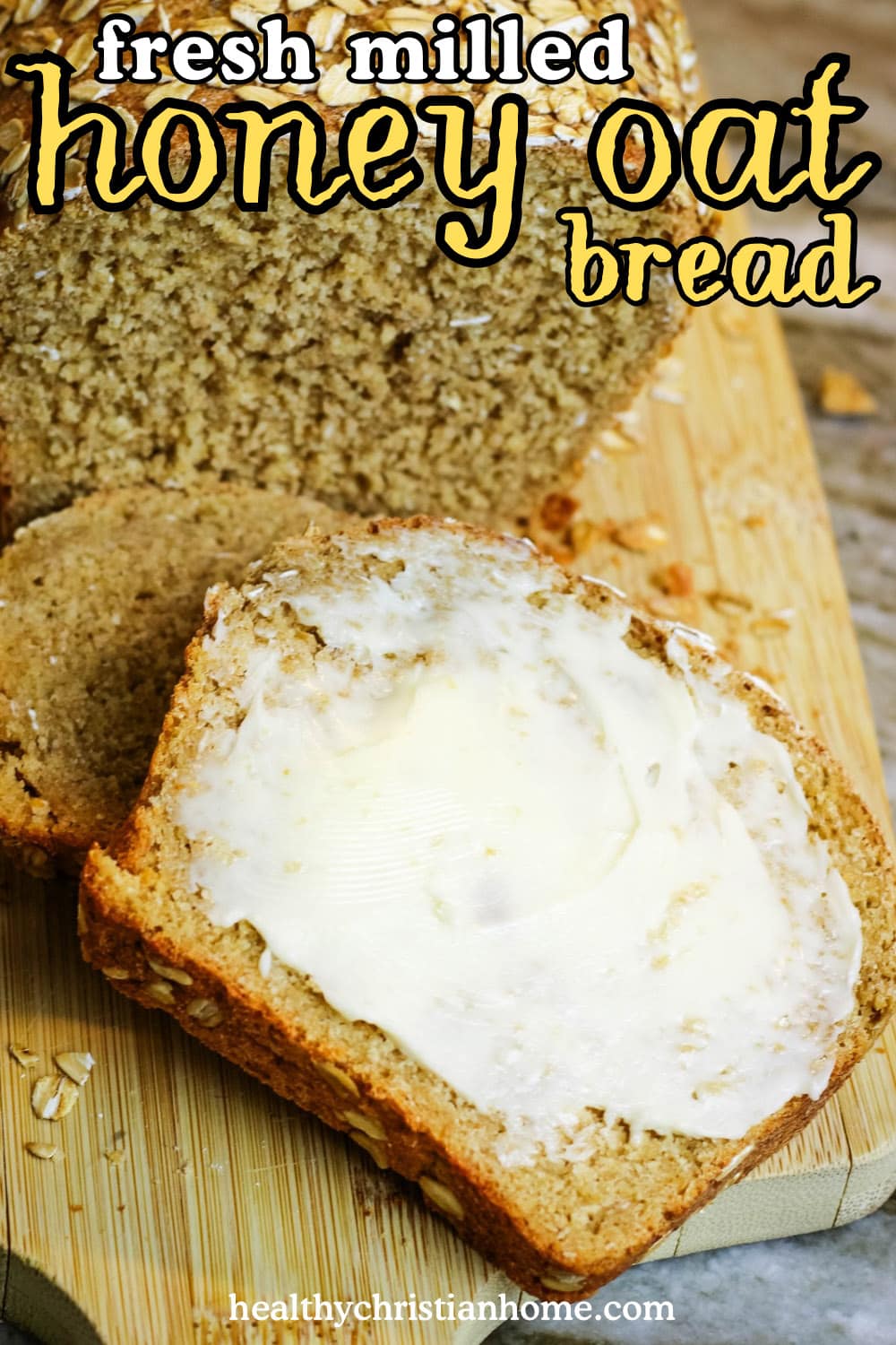 Fresh milled honey oat bread on a cutting board with a buttered slice in front.